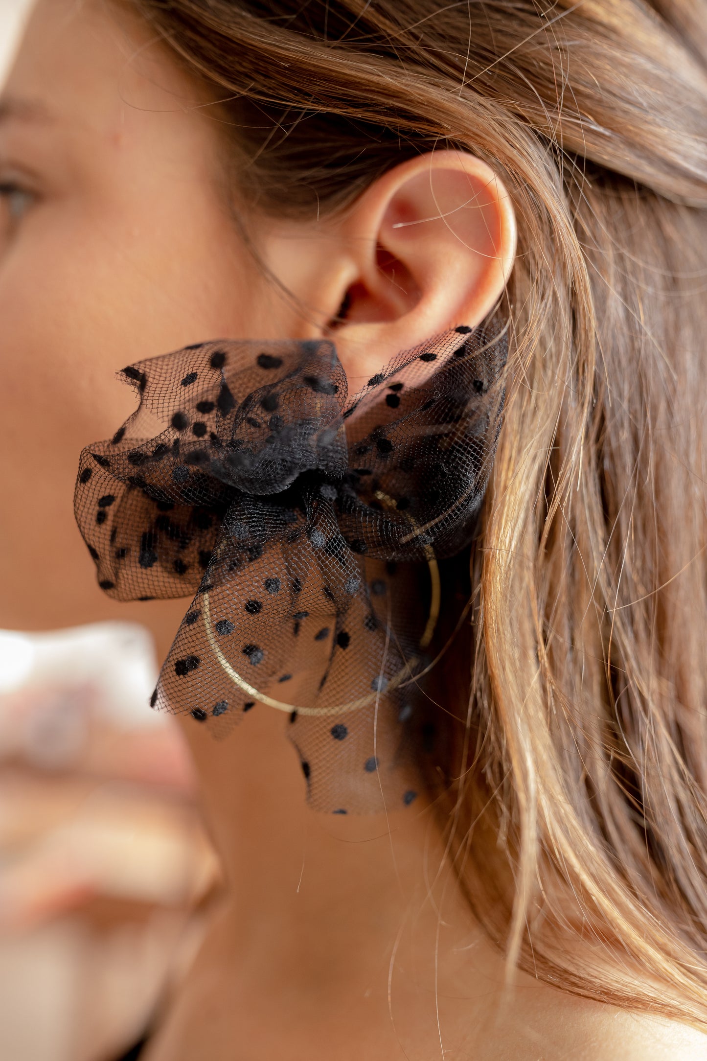 Boucles d’oreilles ornées d’un noeud en plumetis noir autour d’une créole, personnalisables pour oreilles percées ou à clips.