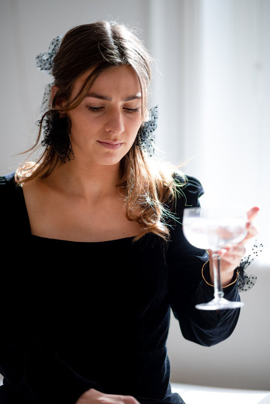 Boucles d’oreilles ornées d’un noeud en plumetis noir autour d’une créole, personnalisables pour oreilles percées ou à clips.